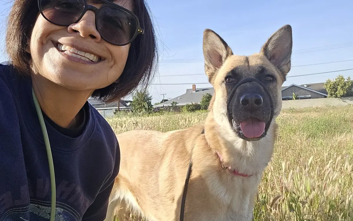 Angelica taking a selfie with a German Shepherd on a walk in a grassy field